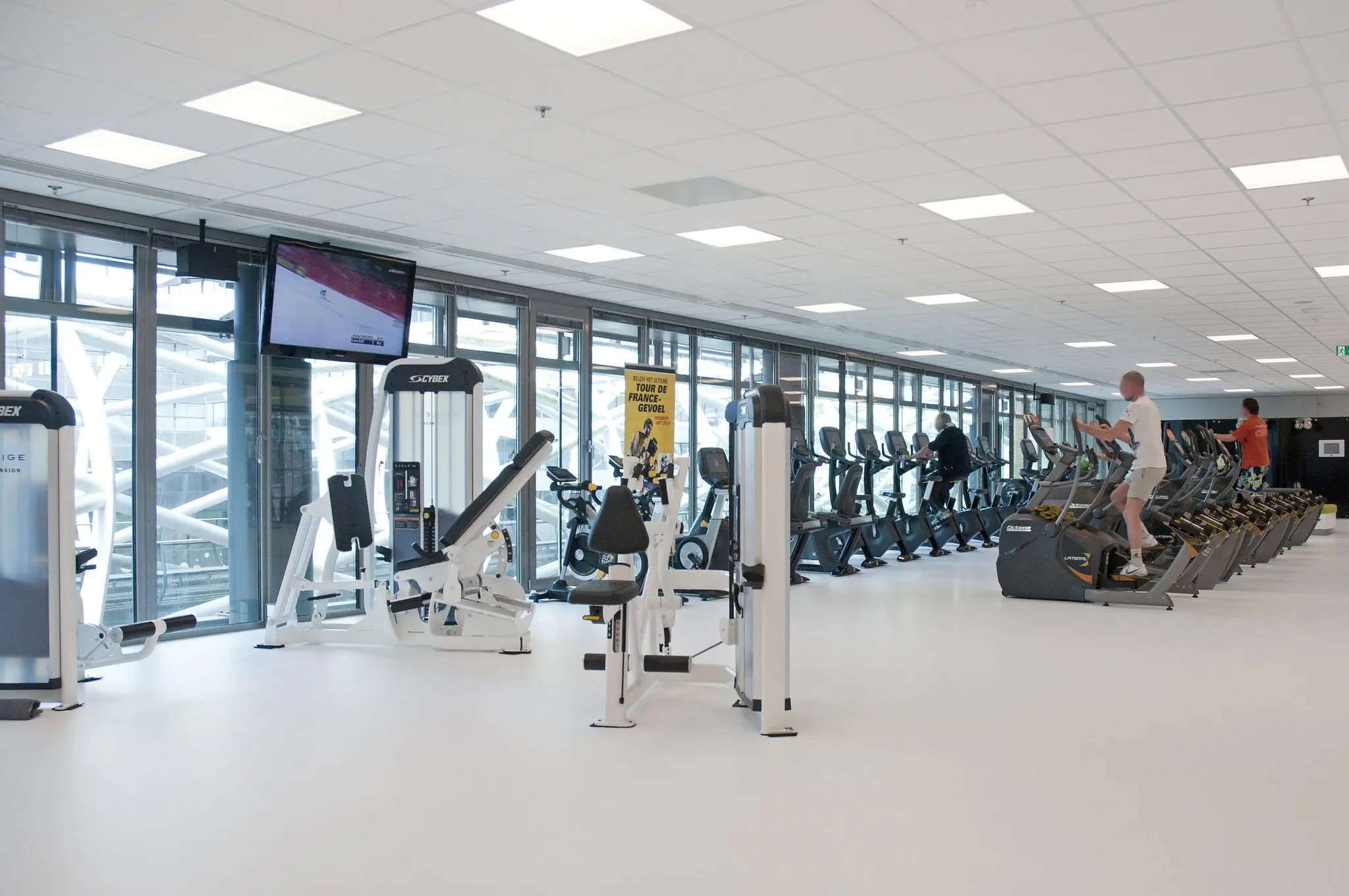 Moderne fitnessruimte aan de Prinses Beatrixlaan met cardio- en krachtapparatuur en grote ramen met uitzicht naar buiten.